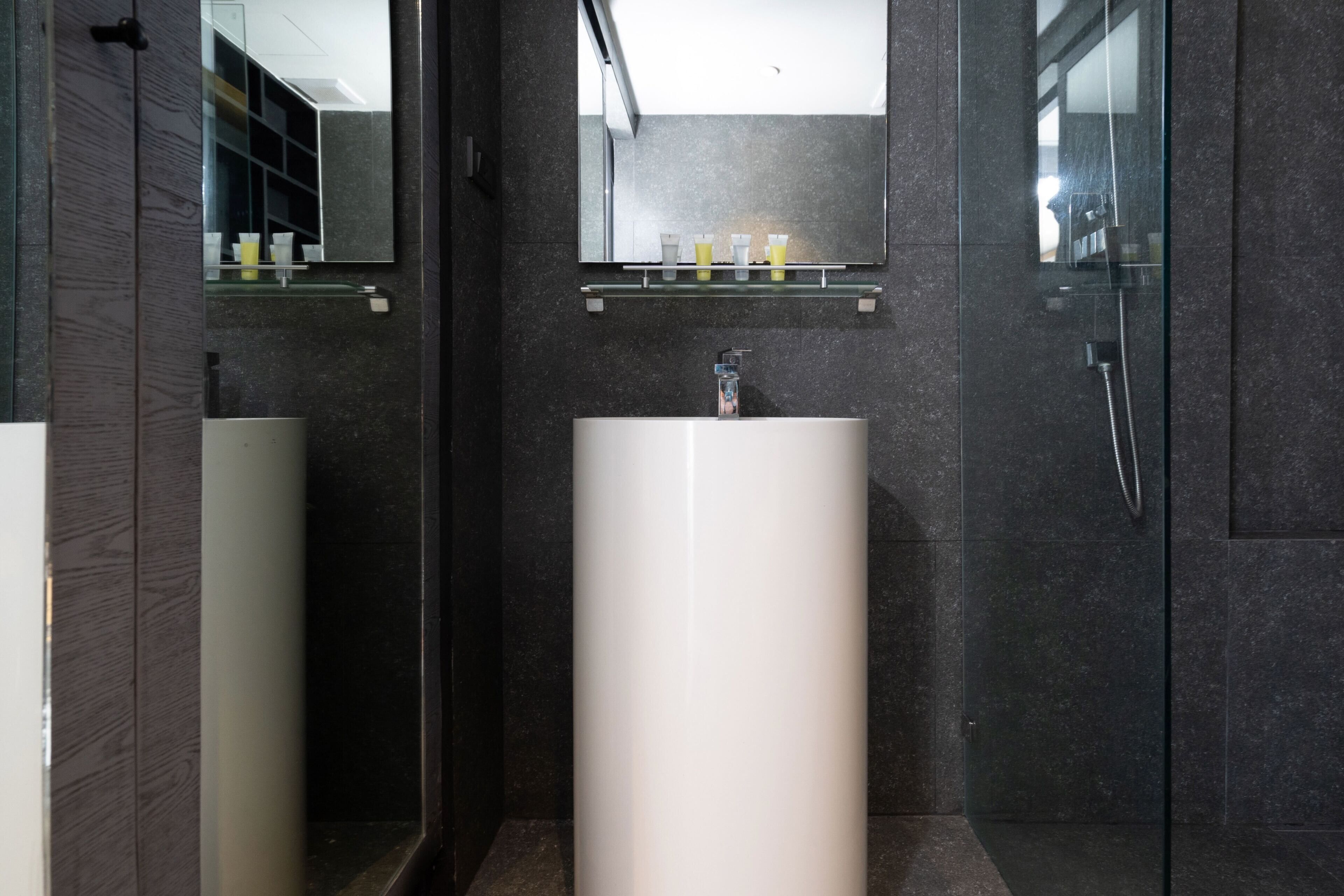 Ein modernes Badezimmer mit einem großen, weißen Waschbecken, einem Spiegel darüber und einer Dusche rechts.