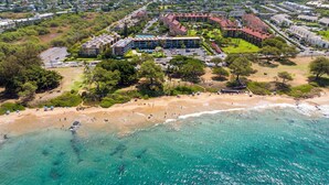 An aerial view of a coastal area with a beach, a hotel complex with multiple buildings, and surrounding greenery. - New Bathrooms! Modern Spacious Penthouse Oceanview (Kihei)