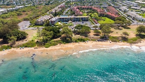 Vista aérea de una zona costera con playa, un complejo hotelero con varias edificaciones y vegetación circundante.