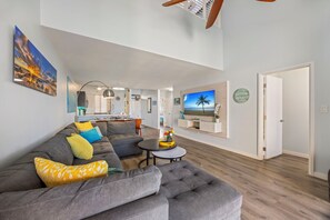 A modern living room with a gray sectional sofa, a round coffee table, and a flat-screen TV mounted on the wall.