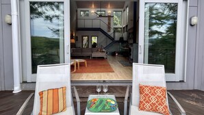 Une porte coulissante s’ouvre sur un vaste espace de vie comprenant un escalier, une table à manger avec des chaises et une vue sur l’extérieur.