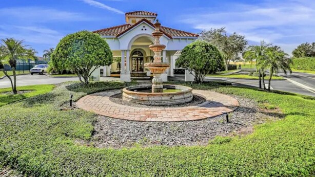 A building with a fountain in the center, surrounded by well-maintained landscaping and a clear sky.
