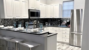 A modern kitchen with white cabinets, a large island with bar stools, a stainless steel refrigerator, and a backsplash with a black and white pattern.
