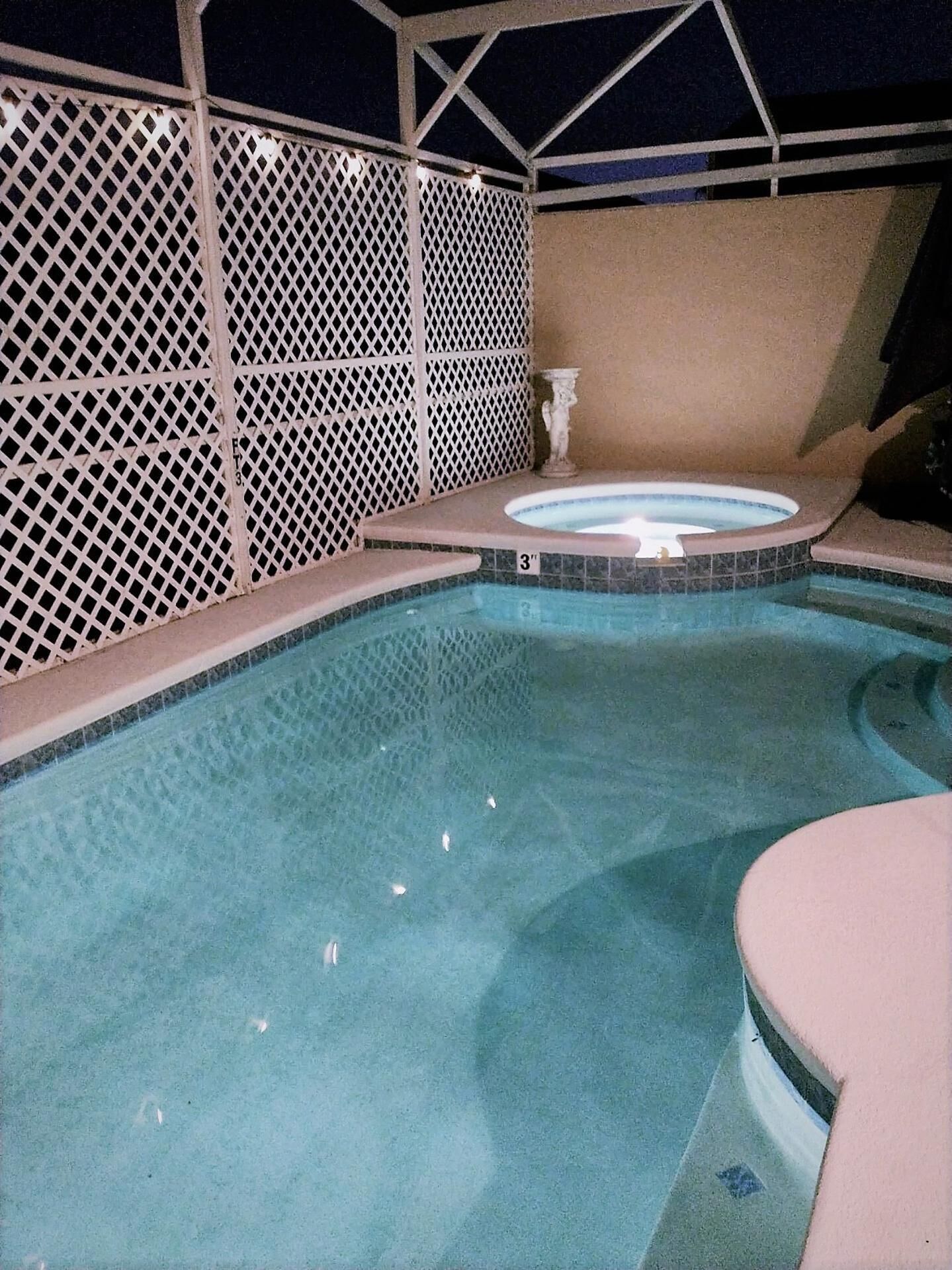Une piscine avec un jacuzzi, le tout entouré d’une clôture en treillis blanc.