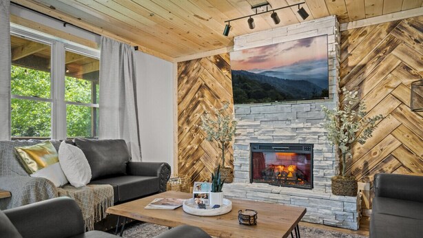 A cozy living room with a stone fireplace, a large window, and a herringbone wood wall.