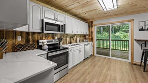 A modern kitchen with white cabinets, stainless steel appliances, and a wooden ceiling.