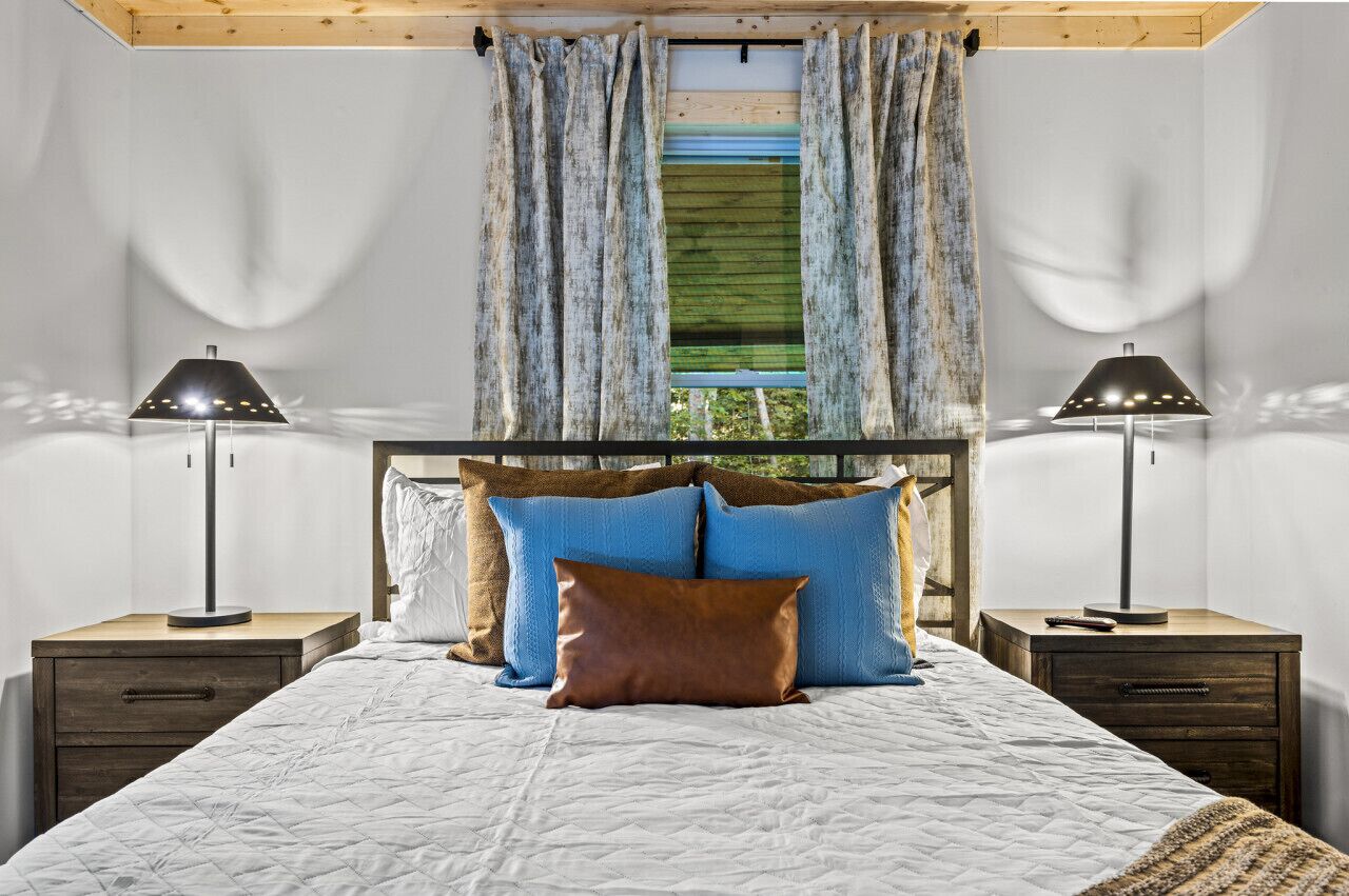 Ein Schlafzimmer mit einem Bett, zwei Nachttischen, einem Fenster mit Vorhängen und Blick auf Grünfläche.
