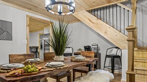 A dining area with a wooden table set for four, a potted plant, and a staircase.
