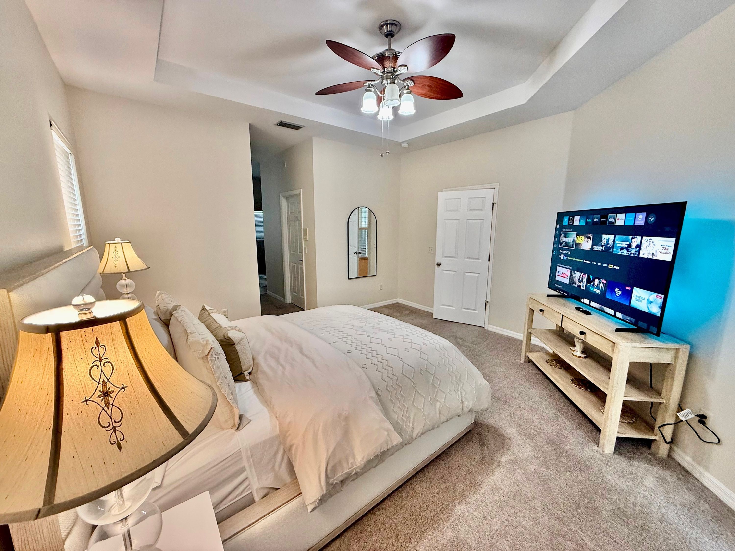 Une chambre à coucher avec un lit, une télévision, un ventilateur de plafond et une lampe.