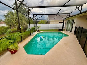 A rectangular pool with a clear blue water surface, surrounded by a covered patio area with a metal frame and glass doors. - Grand Family House With Private Pool Near Disney Parks (Davenport)