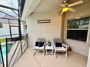 A covered patio area with two wicker chairs, a small table, and a ceiling fan.
