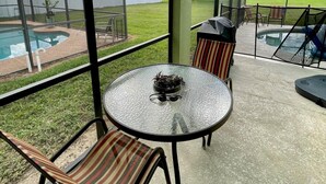 A covered patio with a round table, chairs, and a view of a swimming pool and backyard.