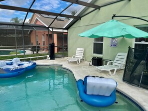An indoor pool area with inflatable loungers, a covered seating area, and a view of the outside building. - Grand Family House With Private Pool Near Disney Parks (Davenport)