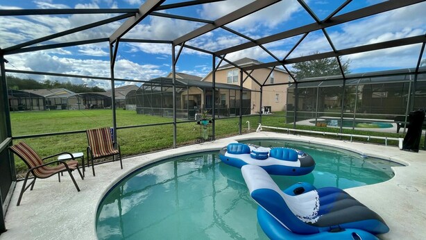 A swimming pool with inflatable loungers, a covered patio area, and a view of a residential neighborhood.