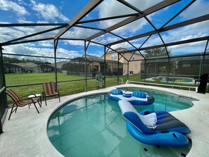 A swimming pool with inflatable loungers, a covered patio area, and a view of a residential neighborhood. - Grand Family House With Private Pool Near Disney Parks (Davenport)