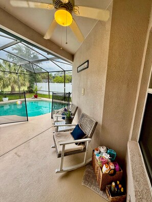 A covered patio area with a pool, outdoor seating, and a ceiling fan.