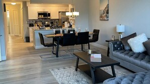 Ein modernes Wohnzimmer mit grauem Sofa, Couchtisch und einem Essbereich mit Stühlen und Tisch.