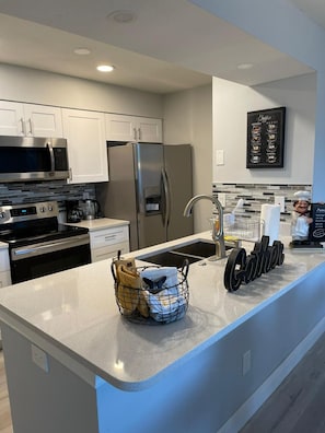 A modern kitchen with white cabinets, stainless steel appliances, a granite countertop, and a coffee menu on the wall. - Grand Executive 3BD Condo Apartment Near Disney Parks 4 (Kissimmee)