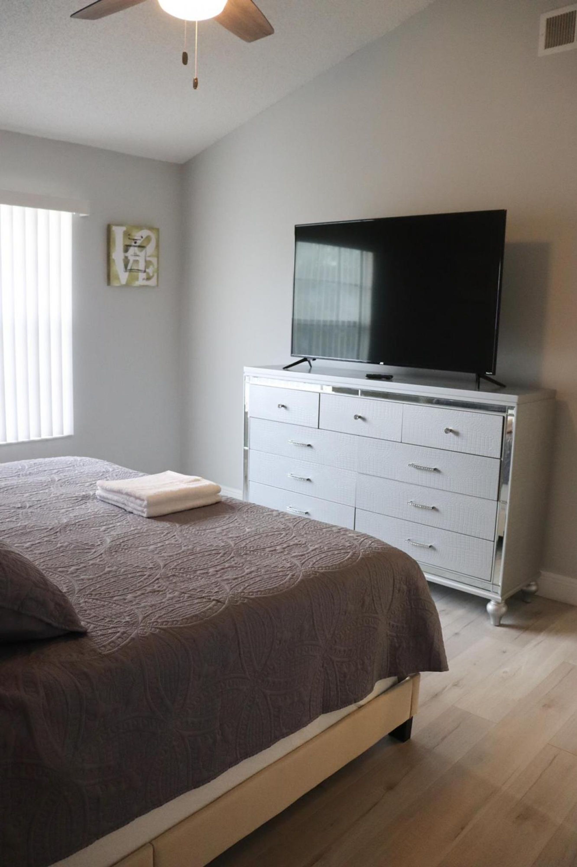 A bedroom with a bed, a dresser, a television, and a ceiling fan.