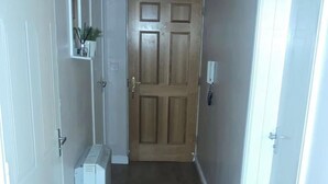 A narrow hallway with a wooden door at the end, a radiator on the left, and a wall-mounted telephone on the right. - Remarkable 2-bed Apartment in London (London)
