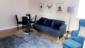A modern living room with a grey sofa, a glass coffee table, and a blue armchair. There are three framed artworks on the wall and a floor lamp. - Remarkable 2-bed Apartment in London (London)