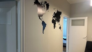 Une pièce dont un mur est décoré d’un grand autocollant représentant une carte du monde, une porte donnant sur une autre pièce, et un coin repas avec une table et des chaises.