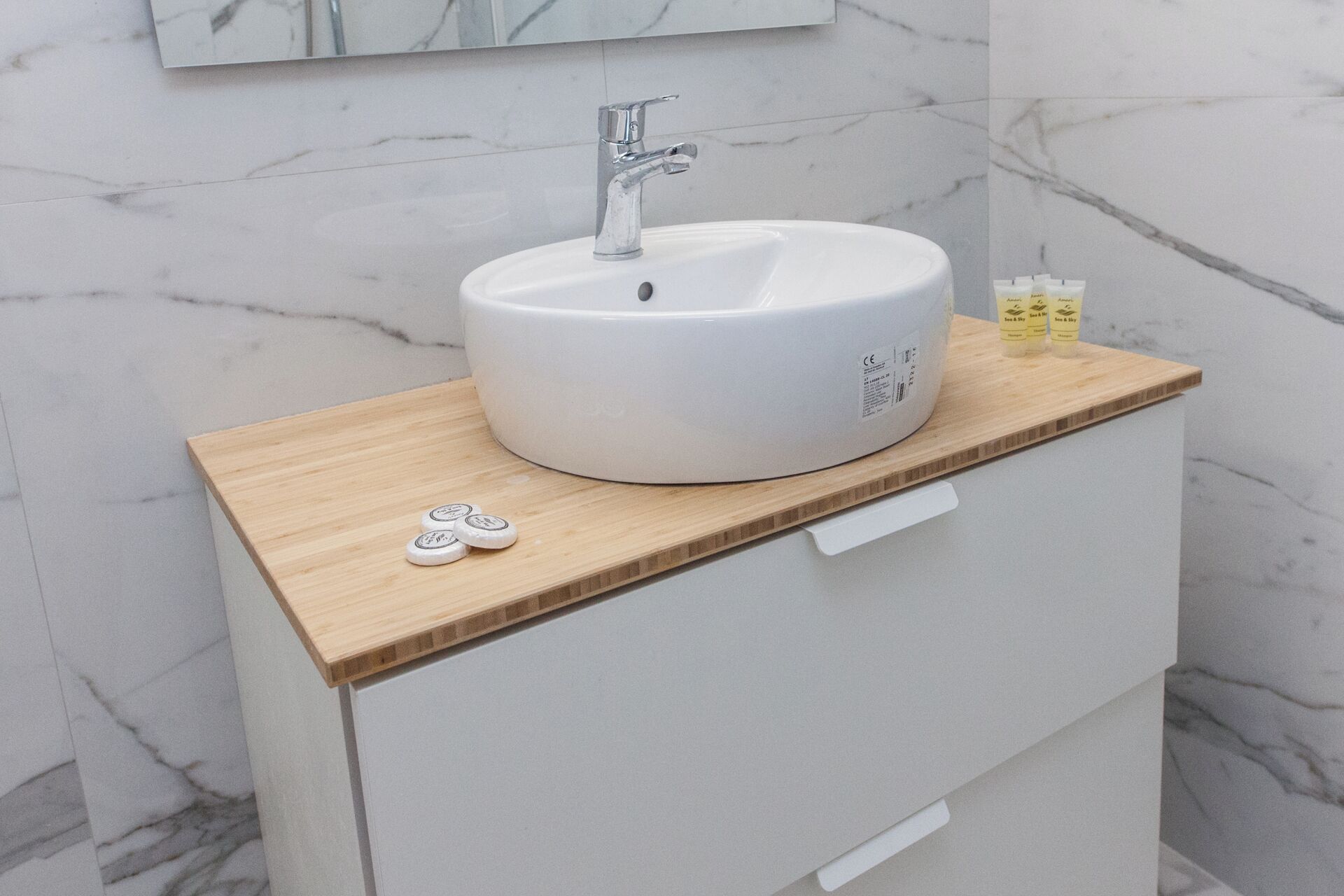 Ein Badezimmer mit einem weißen Waschbecken, einer Holzablage und einer Marmorwand.