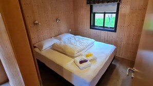 A wooden-paneled room with a bed, a window, and a door. - Minni-Borgir Cabins (Borg)
