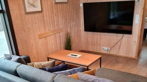 A modern living room with a grey sectional sofa, a wooden coffee table, and a flat-screen TV mounted on the wall. - Minni-Borgir Cabins (Borg)