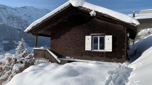 Eine Holzchalet mit schneebedecktem Dach, einem Fenster mit Fensterläden und einer Holzterrasse.