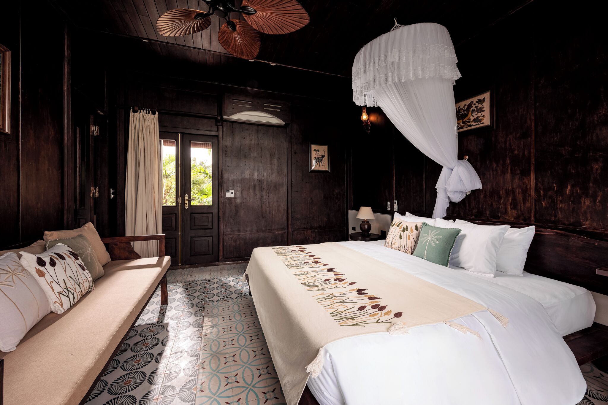 A bedroom with a bed, a sofa, a wooden floor, and a door.
