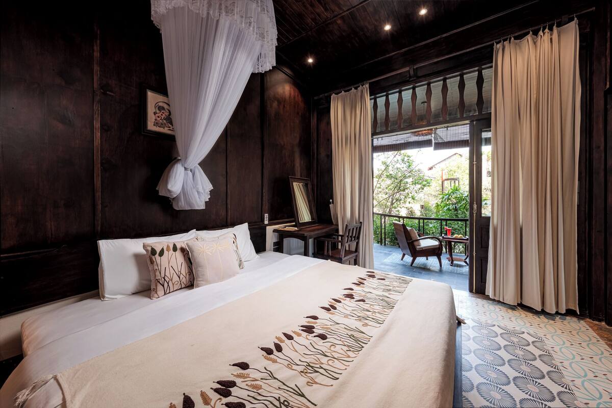 A bedroom with a large bed, a desk, a chair, and a balcony with curtains.