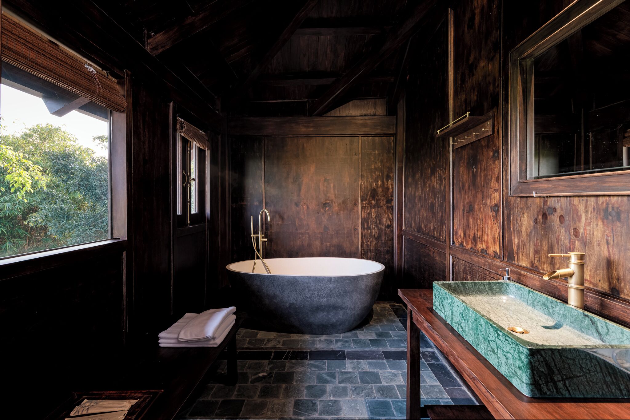 Un bagno con una vasca freestanding, un lavabo con piano in marmo verde e pareti in legno.