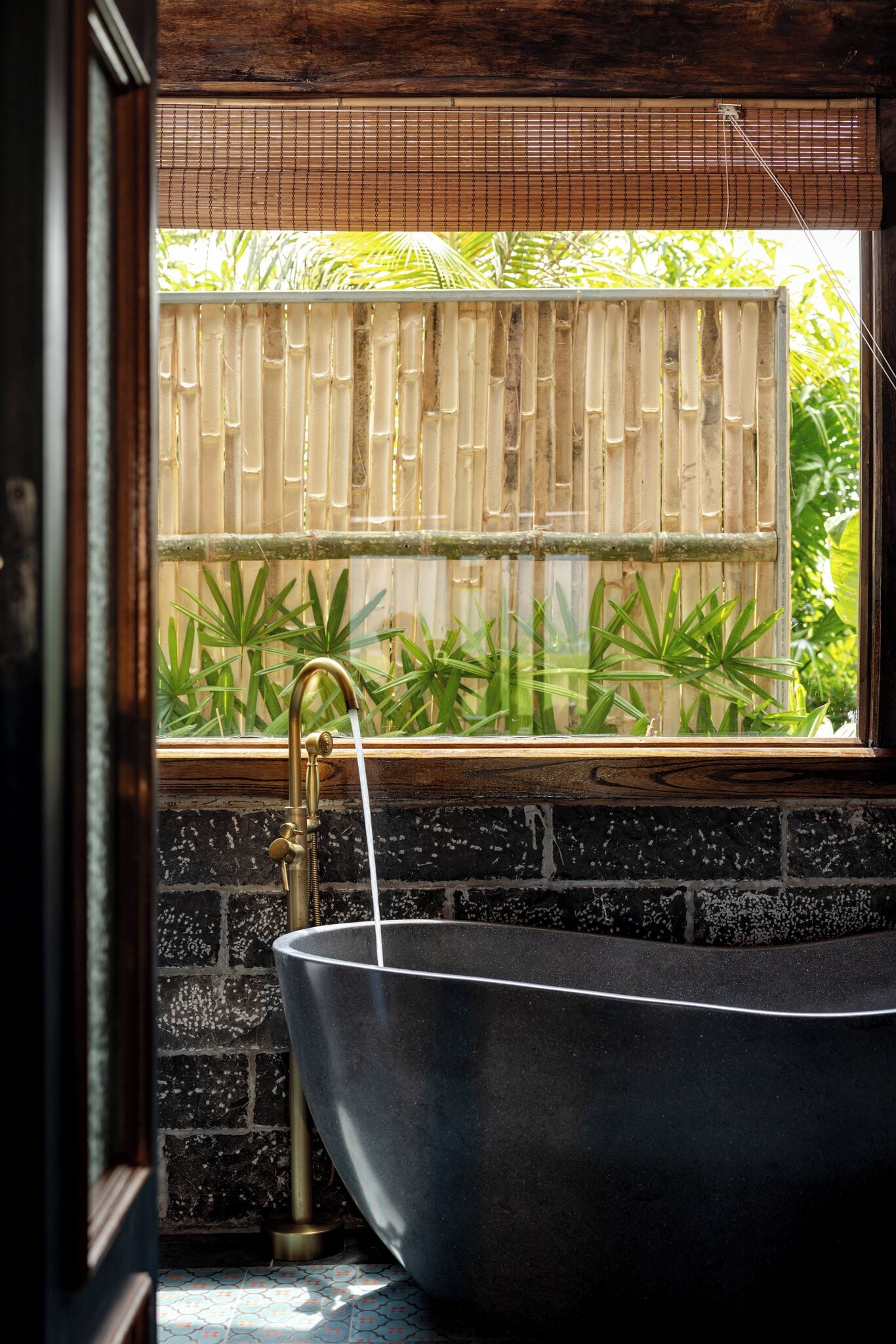 Un bagno con una vasca freestanding, tende in bambù e piante verdi visibili dalla finestra.