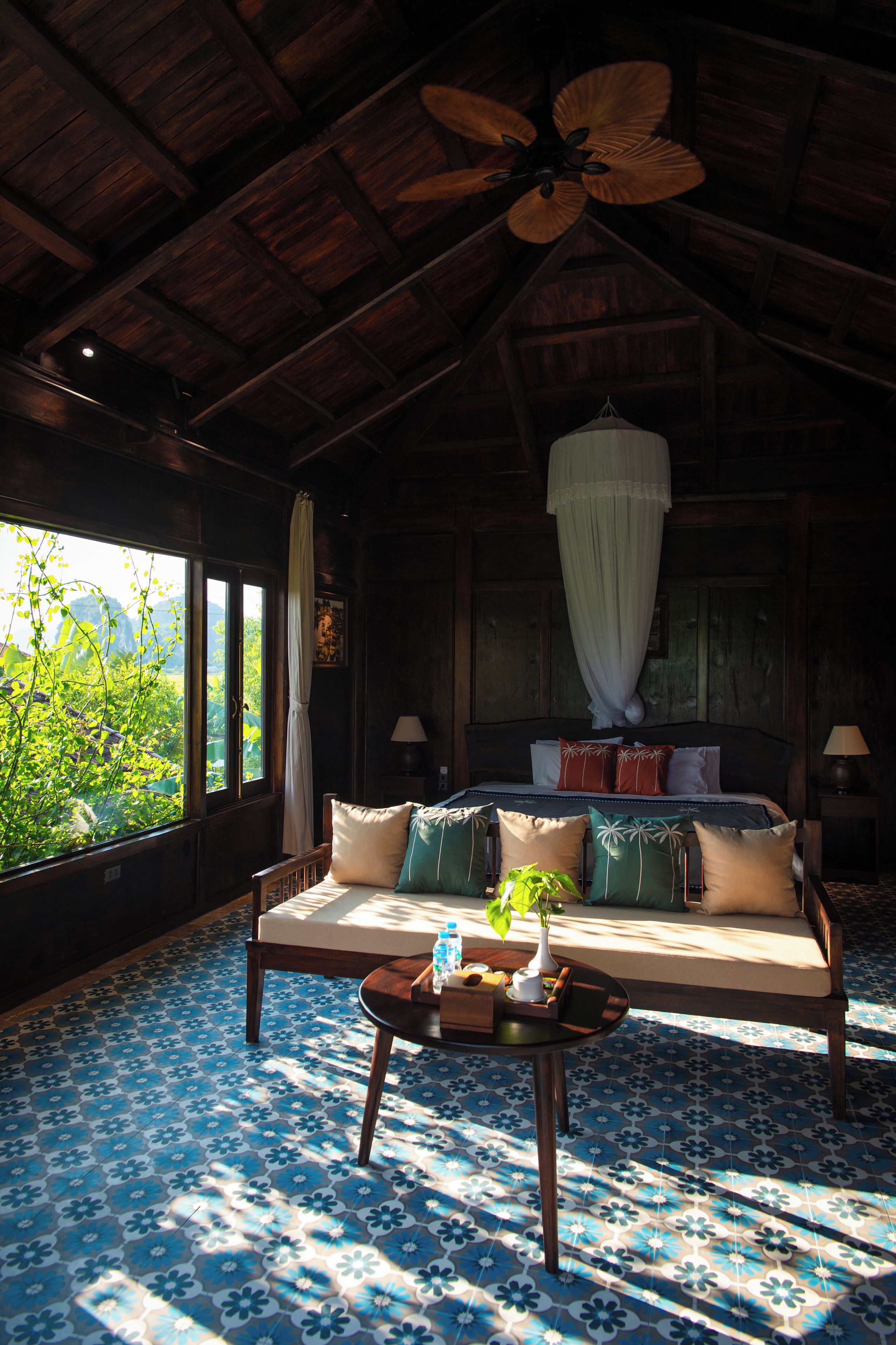 A room with a bed, a sofa, a table, and a ceiling fan.