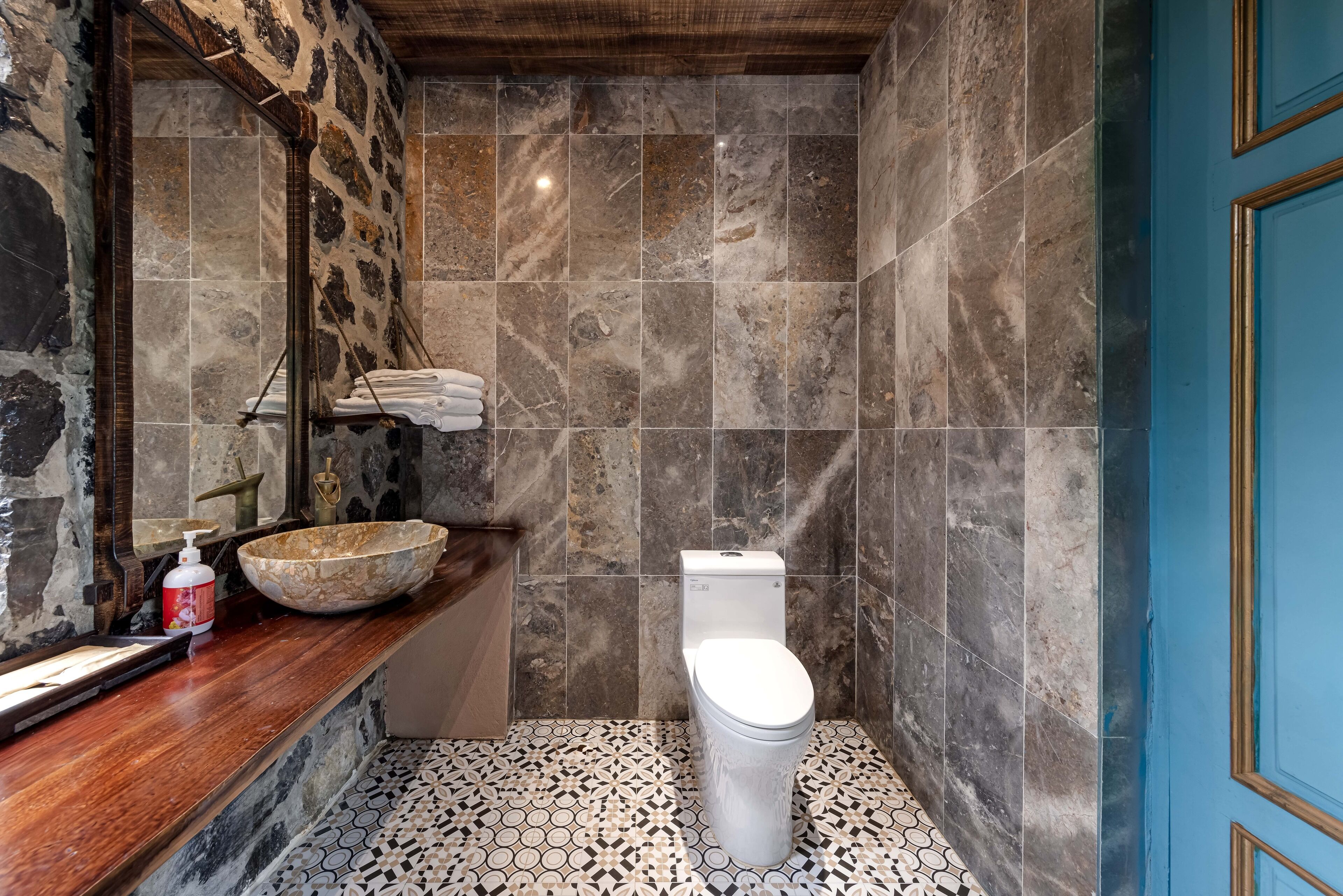 A bathroom with a stone sink, a toilet, and a blue door.