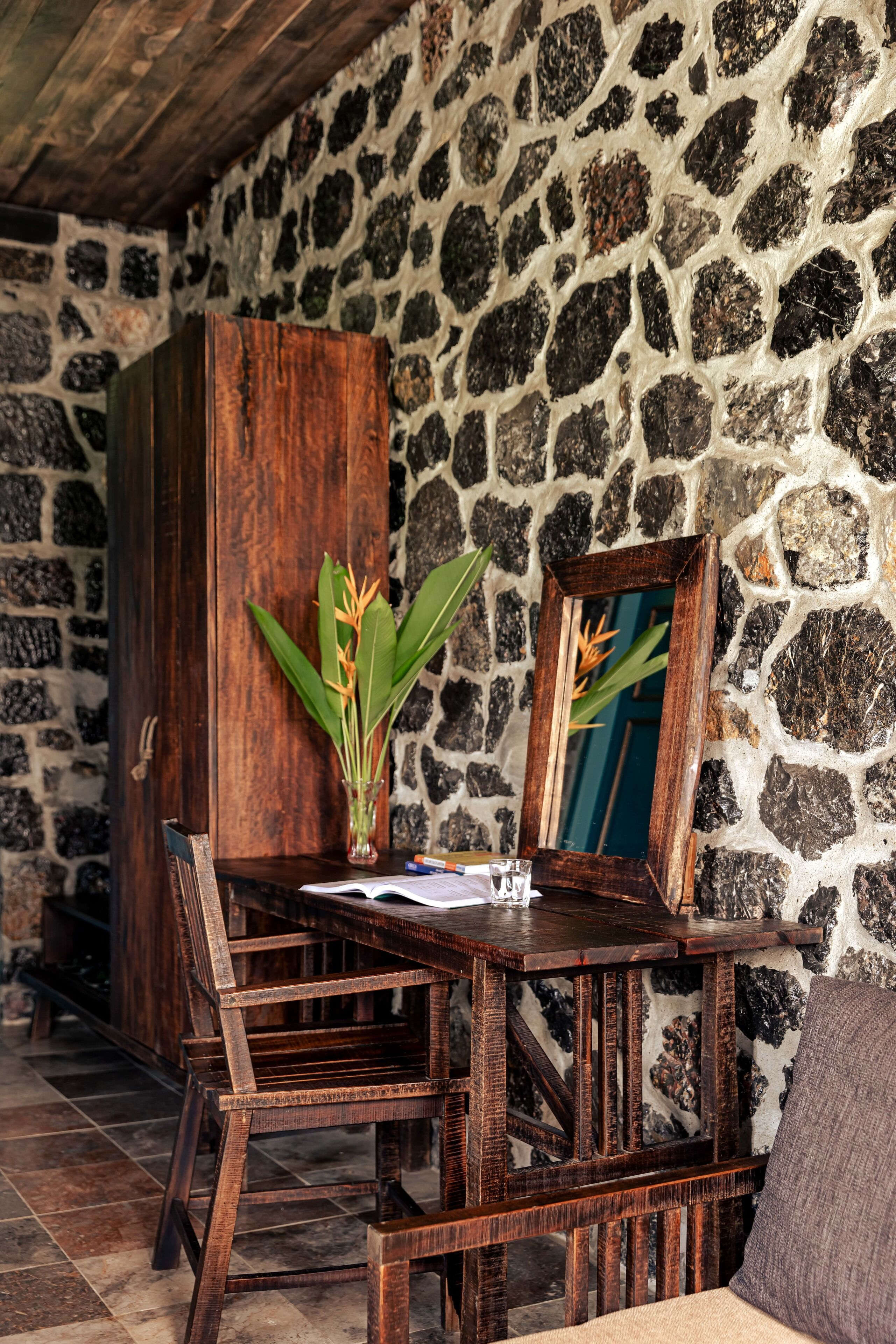 A rustic wooden dining table with chairs, a vase with a plant, and a framed picture on the wall.