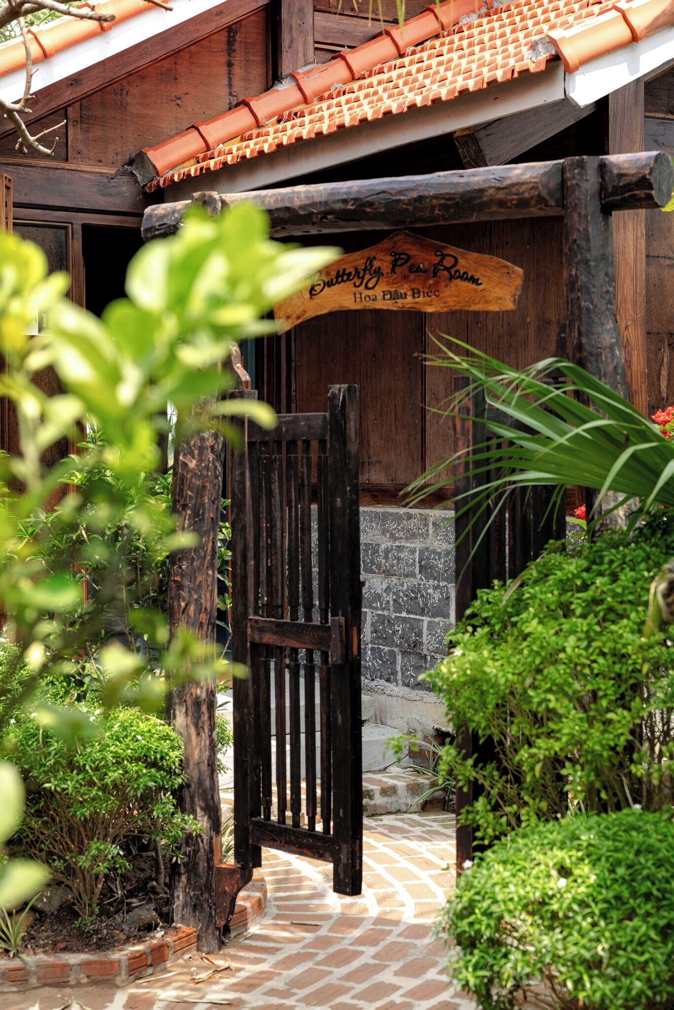 A wooden gate leading to a building with a tiled roof and a sign reading "Butterfly Per Room."
