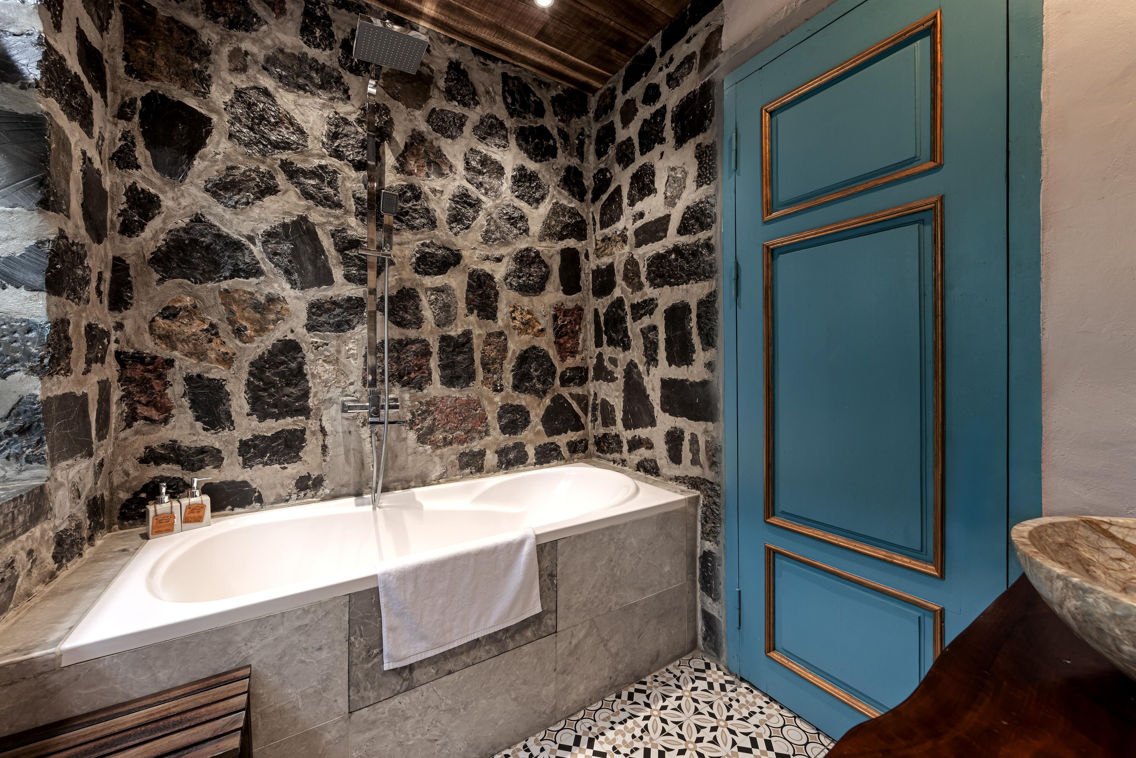 Een badkamer met een stenen muur, een wit bad en een blauwe deur.