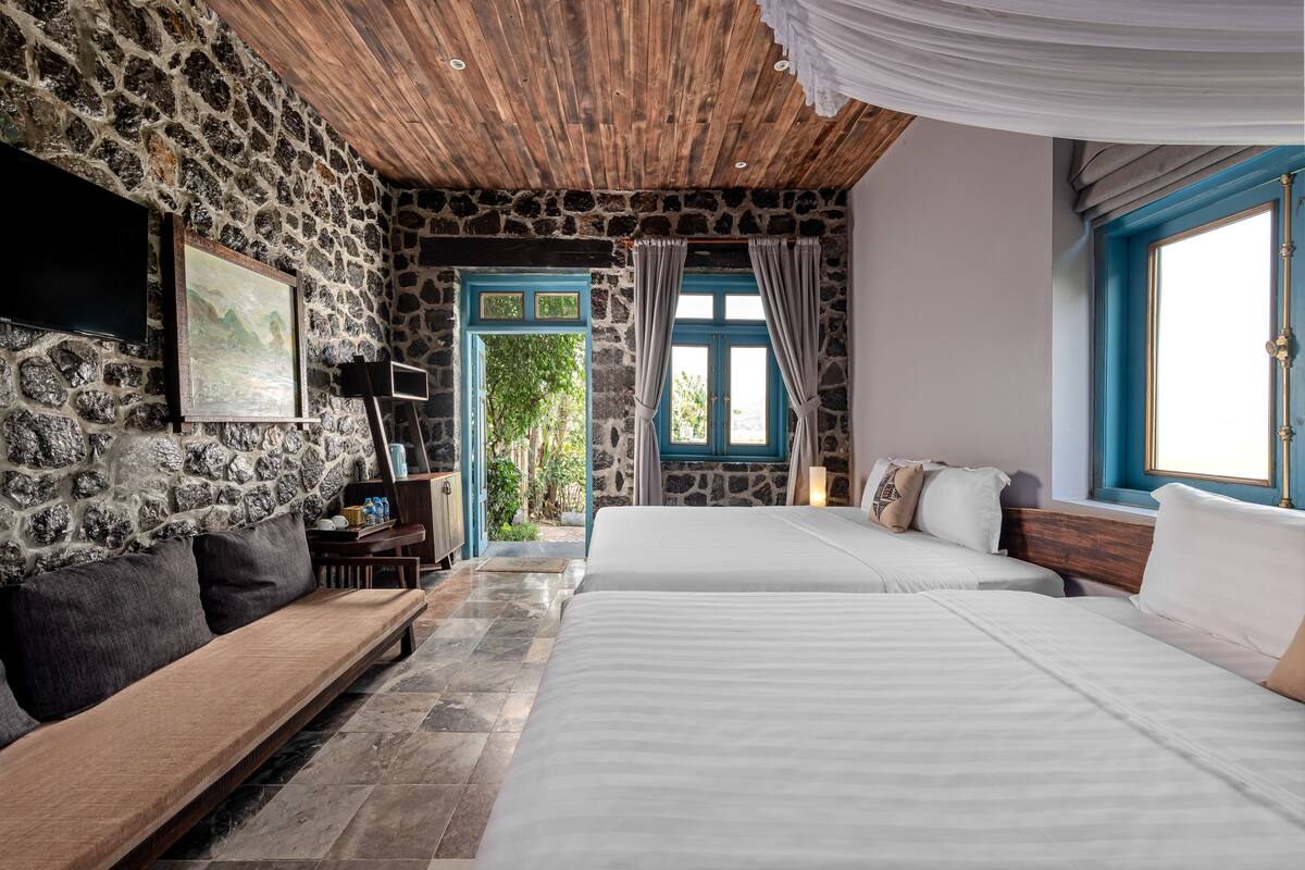 A room with stone walls, wooden ceiling, a bed, a sofa, and a TV.