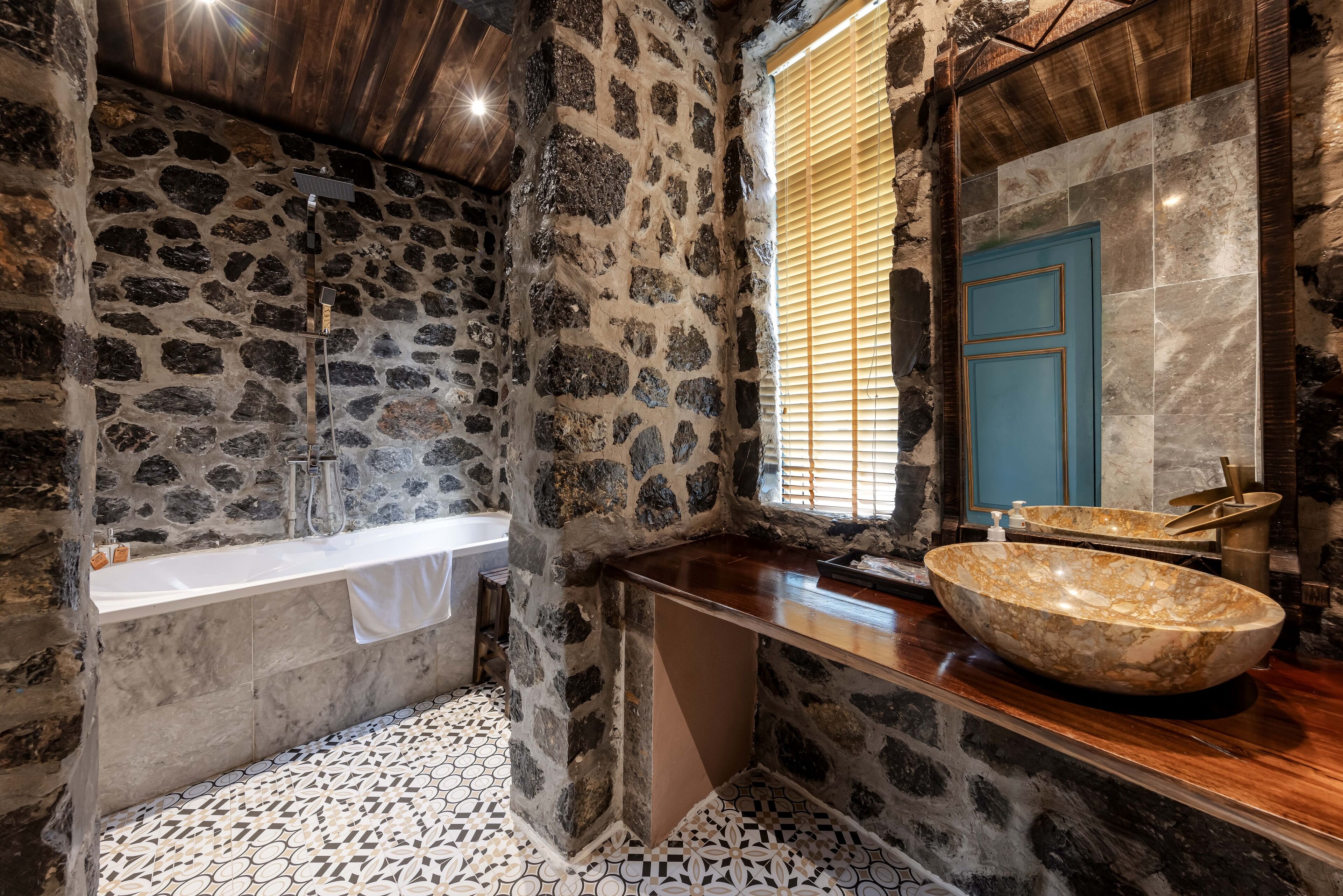 A bathroom with a stone wall, a bathtub, a sink with a large bowl, and a blue door.