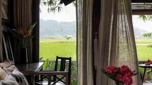 Una habitación con sofá, una mesa con un jarrón de flores y vistas a un campo verde a través de cortinas translúcidas.