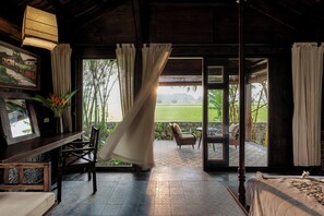 A room with a wooden ceiling, a bed, a table with chairs, and a view of a garden through a glass door. - ChezCao Rice Field Ecolodge Ninh Binh (Hoa Lu)
