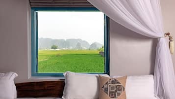 Une chambre avec une grande fenêtre, un lit avec une literie blanche, et une vue sur un champ verdoyant et des collines.