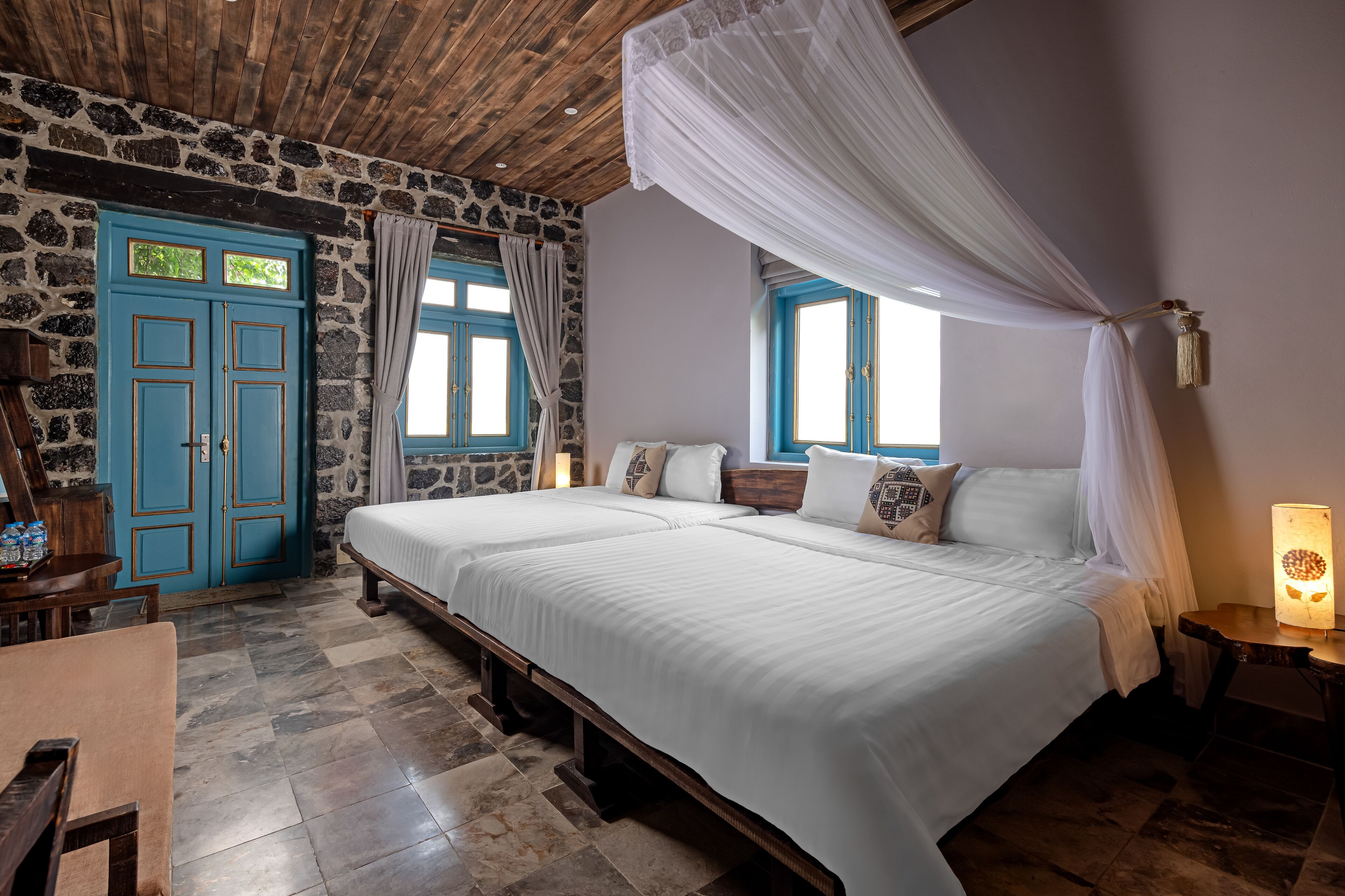 Un dormitorio con dos camas, paredes de piedra, techo de madera y un amplio ventanal con cortinas.