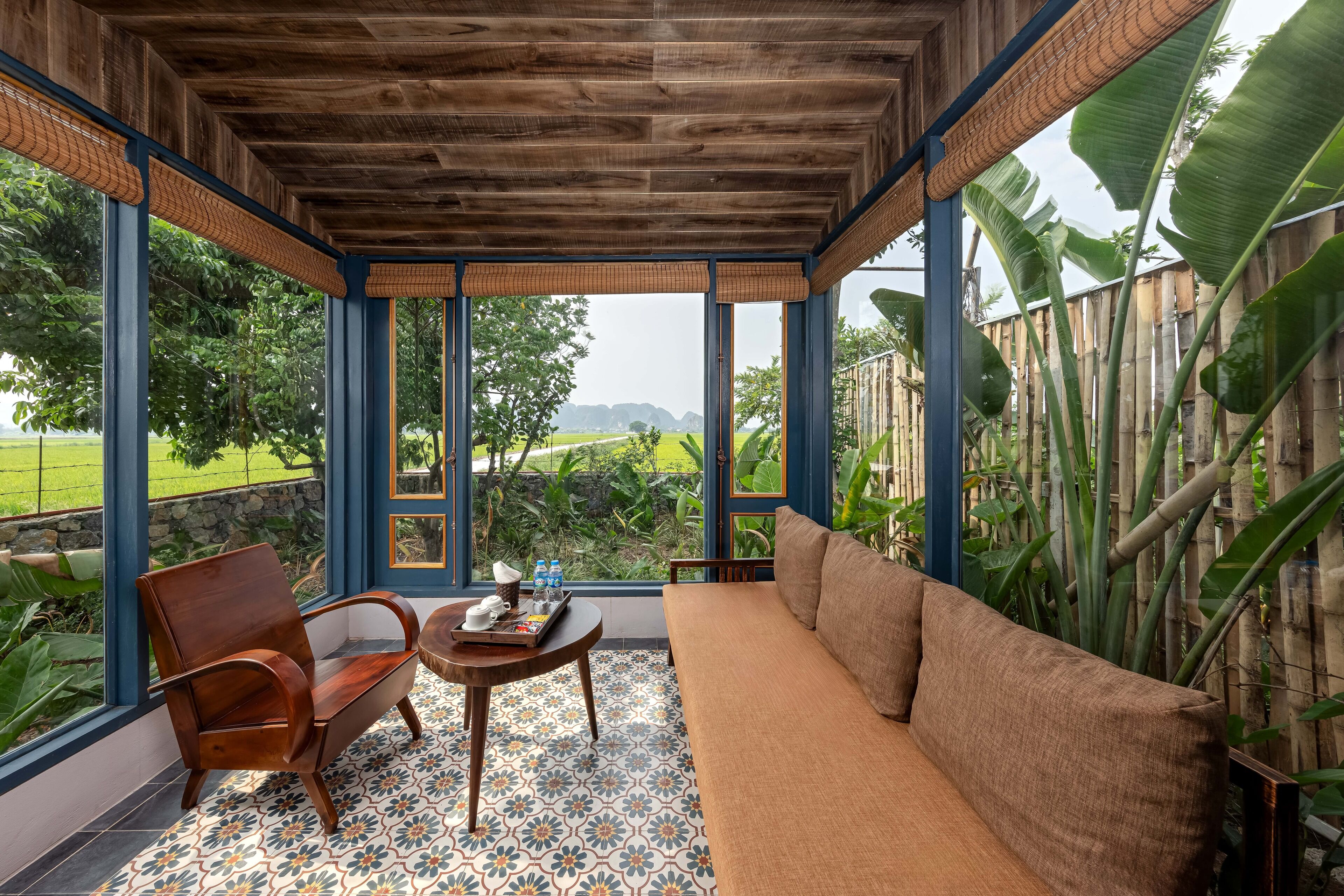 A room with a wooden ceiling, large windows, a sofa, a chair, and a table with a tray.