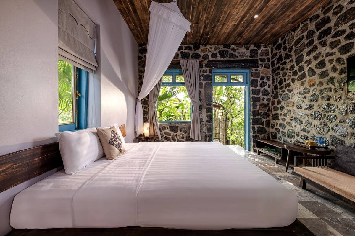 A large bed with white linens, a stone wall, and a wooden ceiling.