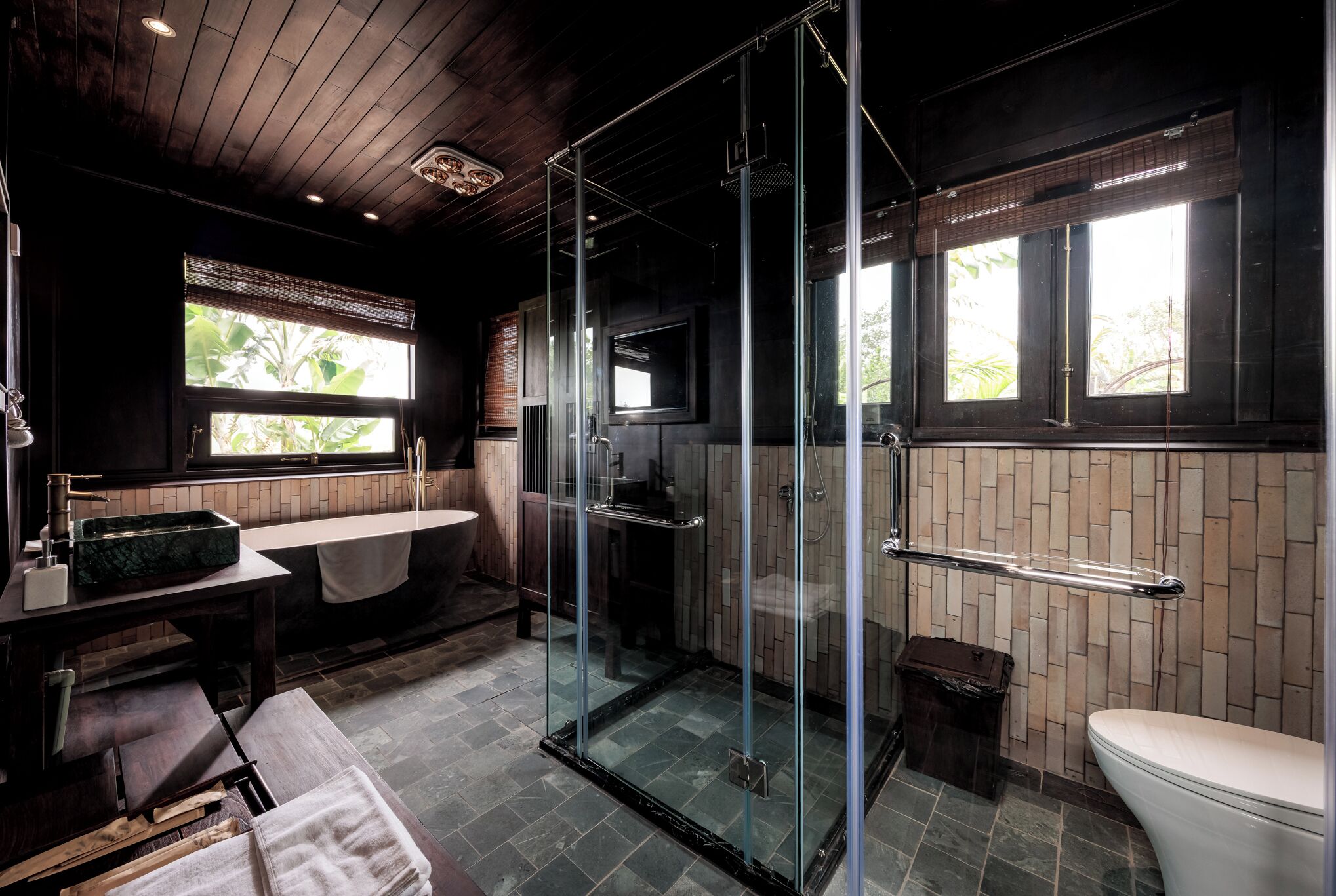 A modern bathroom with a glass shower enclosure, a large window, and a wooden ceiling.