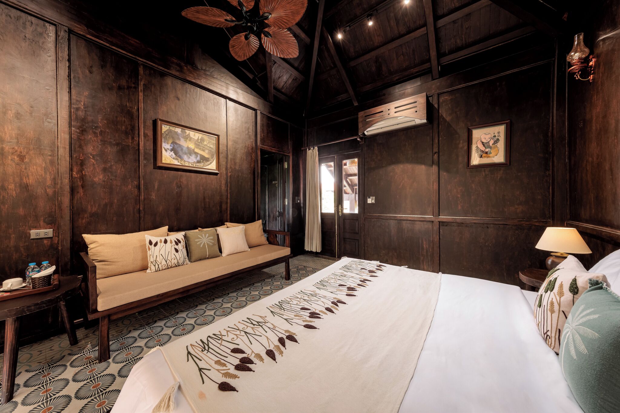 A room with a bed, a sofa, a small table, and a wall-mounted air conditioner.