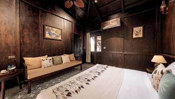 A room with a bed, a sofa, a small table, and a wall-mounted air conditioner.